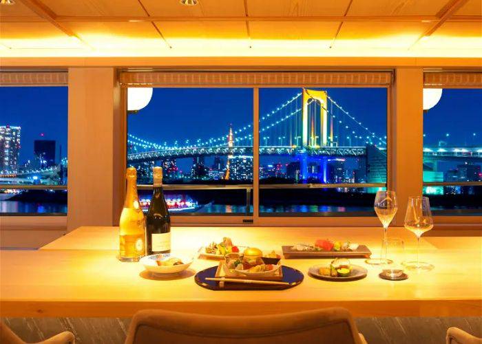 A table laid with a kaiseki multi-course meal and wine, looking out at Tokyo Bay from a yakatabune cruise.